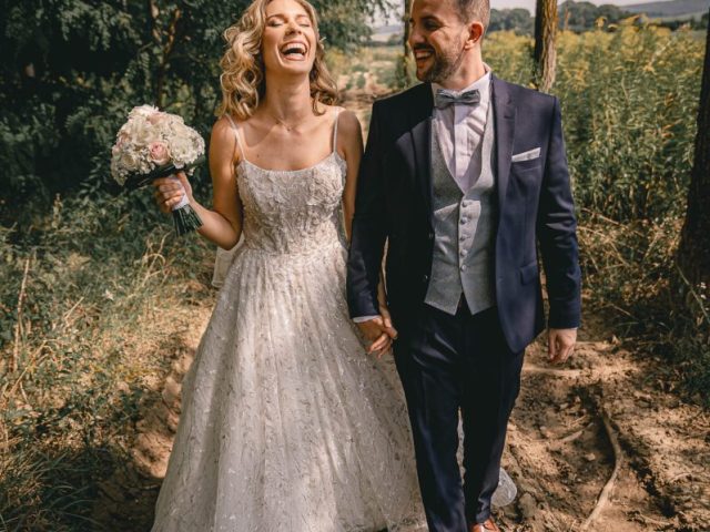 A boldog pár kézen fogva sétál az esküvői fotózáson, festői erdei környezetben.