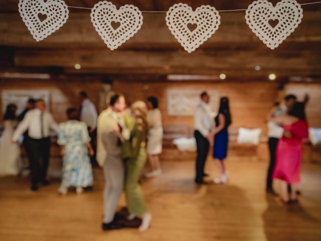 Zaostrené visí šnúra bielych papierových srdiečok, zatiaľ čo niekoľko párov spolu tancuje v jemne osvetlenej miestnosti, rozmazanej v pozadí.