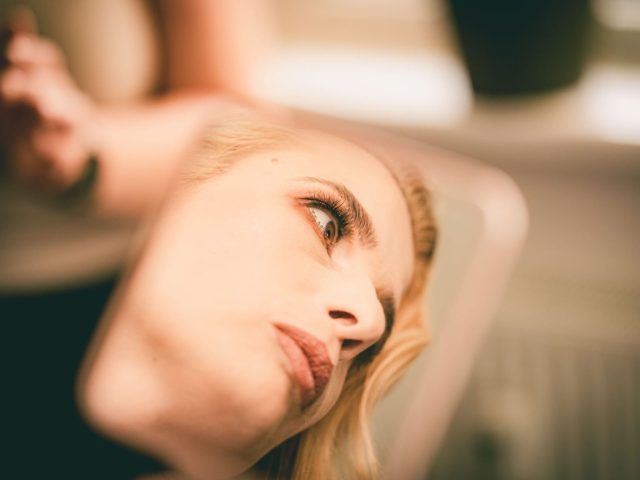 Detailný odraz ženskej tváre v zrkadle, na ktorom sú vidieť jej oči, nos a pery s mäkkým zaostrením a teplým osvetlením. Jej výraz sa zdá byť zamyslený a introspektívny.